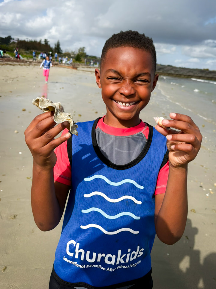 両手に大きな貝殻を持って満面の笑顔を見せる男の子